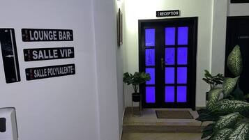 Un área de recepción con un cartel que indica 'RECEPTION' sobre una puerta. Hay letreros que dicen 'LOUNGE BAR', 'SALLE VIP' y 'SALLE POLYVALENTE' en la pared.