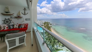 A balcony with a view of a beach, a red sofa, a small table, and decorative maritime items.