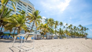 A beach with a soccer goal, palm trees, and a hotel in the background.