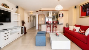 A modern living room with a TV, sofa, coffee table, and kitchen in the background.