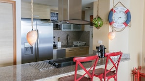 A modern kitchen with granite countertops, stainless steel appliances, and red bar stools.