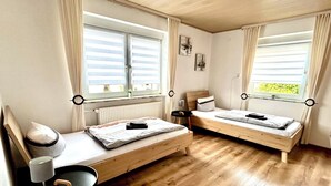 A room with two wooden beds, a small table, a chair, and a radiator.