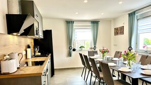 A modern kitchen with a dining area, featuring a wooden countertop, a built-in oven, and a dining table set for six with chairs.