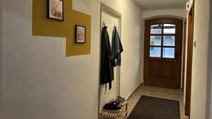 A hallway with a wooden door, a coat rack with jackets, and a shoe rack with sneakers.