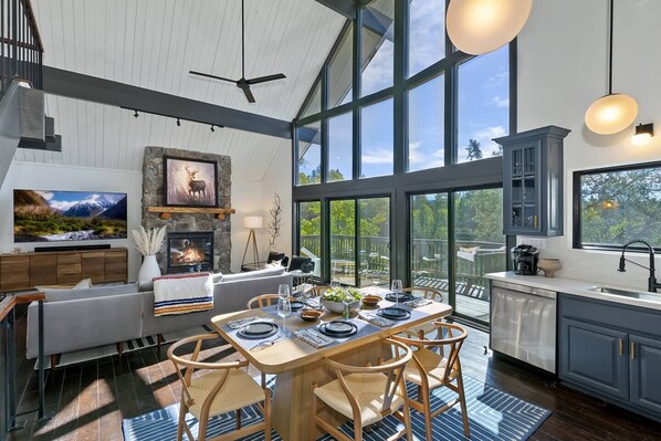 A modern kitchen with a dining area, large windows, and a fireplace.