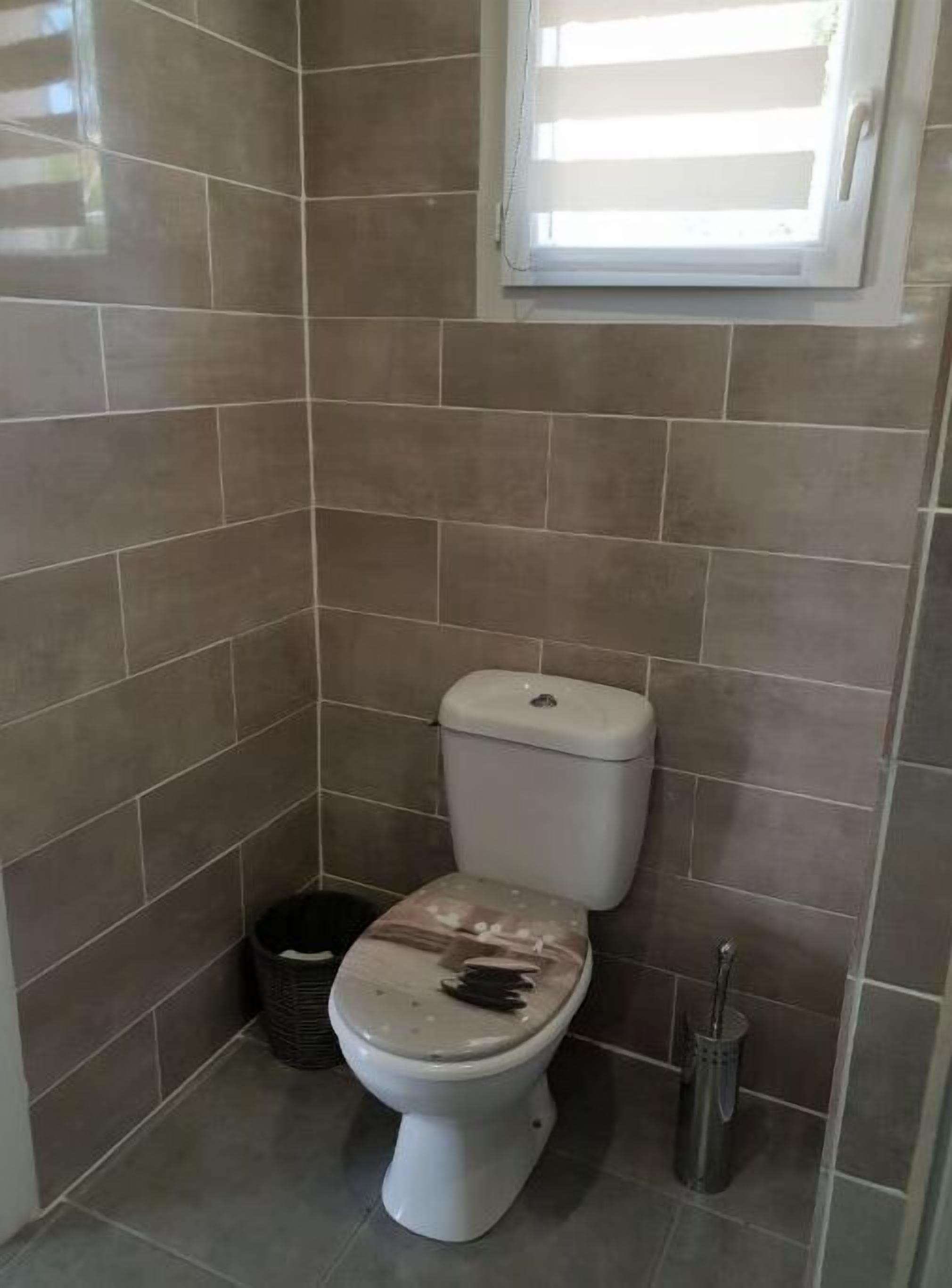 Un baño pequeño con un inodoro, un cesto de basura y una ventana.
