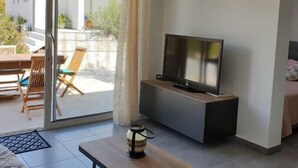 A modern living room with a TV, a coffee table, and a sliding glass door leading to an outdoor area with a table and chairs. - Maison de Campagne, en Pleine Nature (Sari-Solenzara)