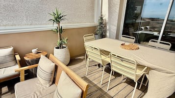 Un espace extérieur ensoleillé, aménagé avec une terrasse en bois, des fauteuils confortables, une table ronde et des plantes en pot.