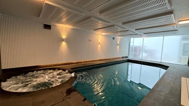 A swimming pool with a textured wall and ceiling vents, a clear view of the sky, and a tiled floor.