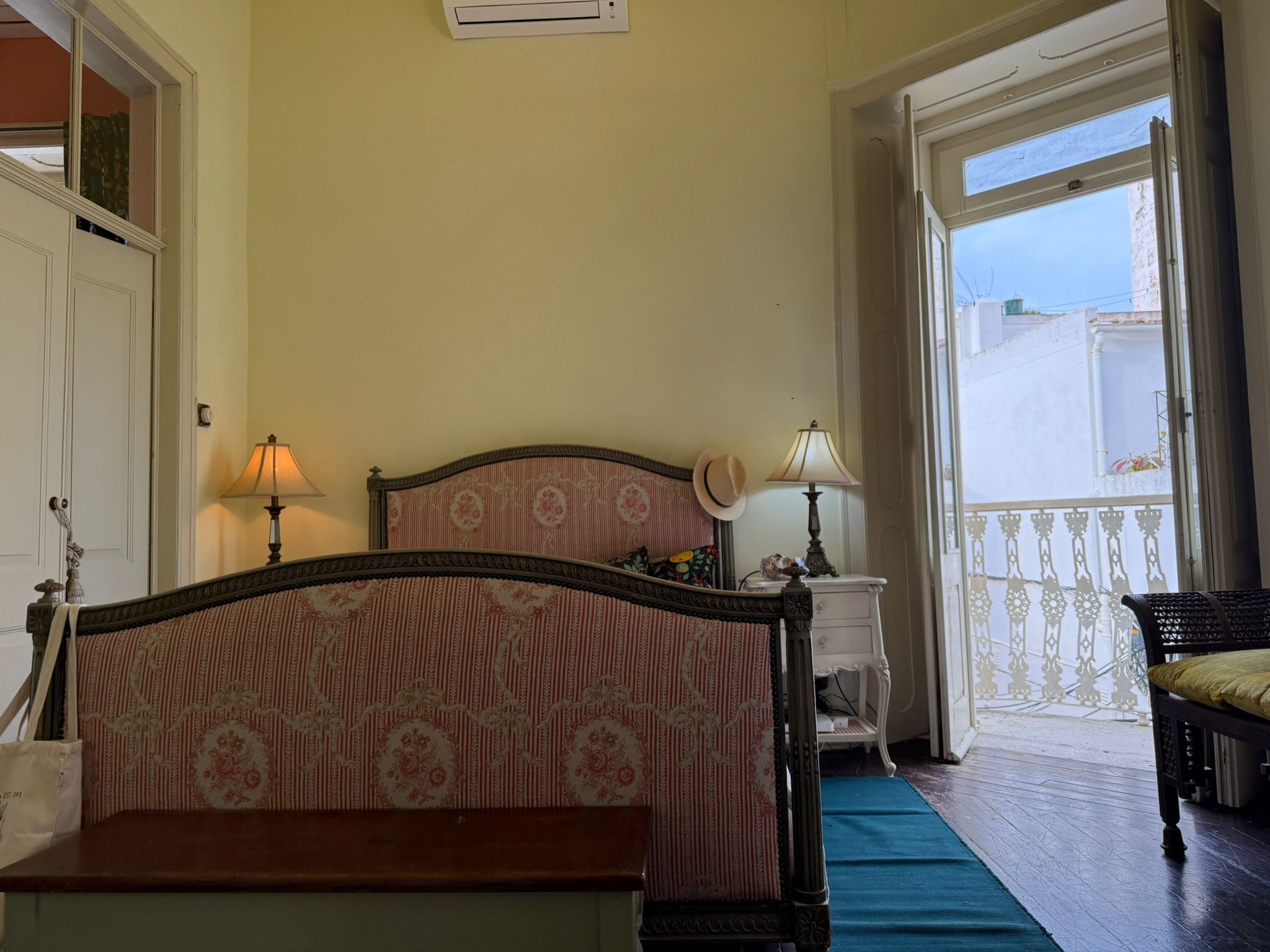 Quarto com cama, duas luminárias de cabeceira, mesa de cabeceira, uma cadeira e vista para a varanda.