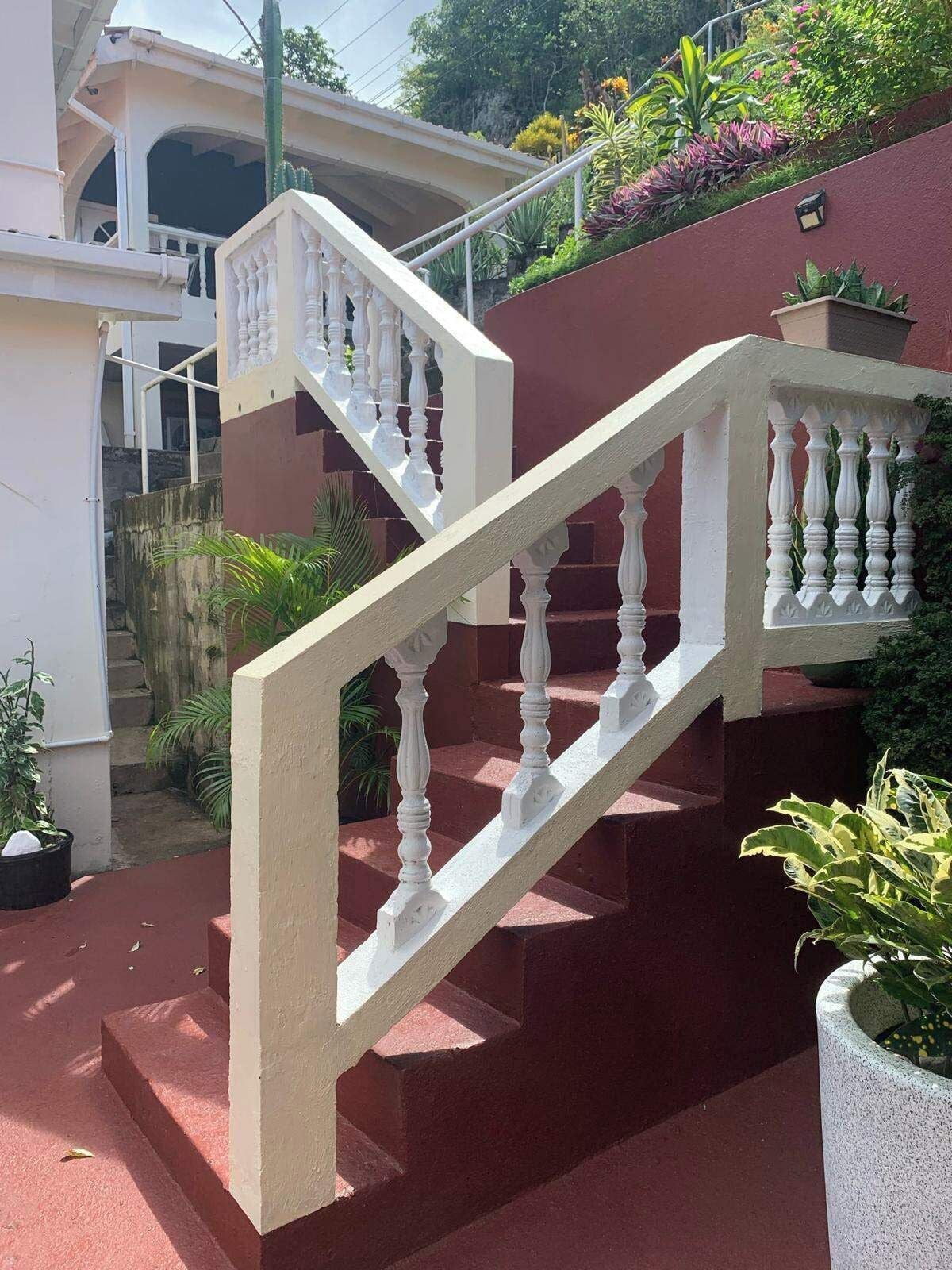 A staircase with white balusters leading to a landing, surrounded by greenery and a building facade.