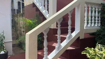 A staircase with white balusters leading to a landing, surrounded by greenery and a building facade.