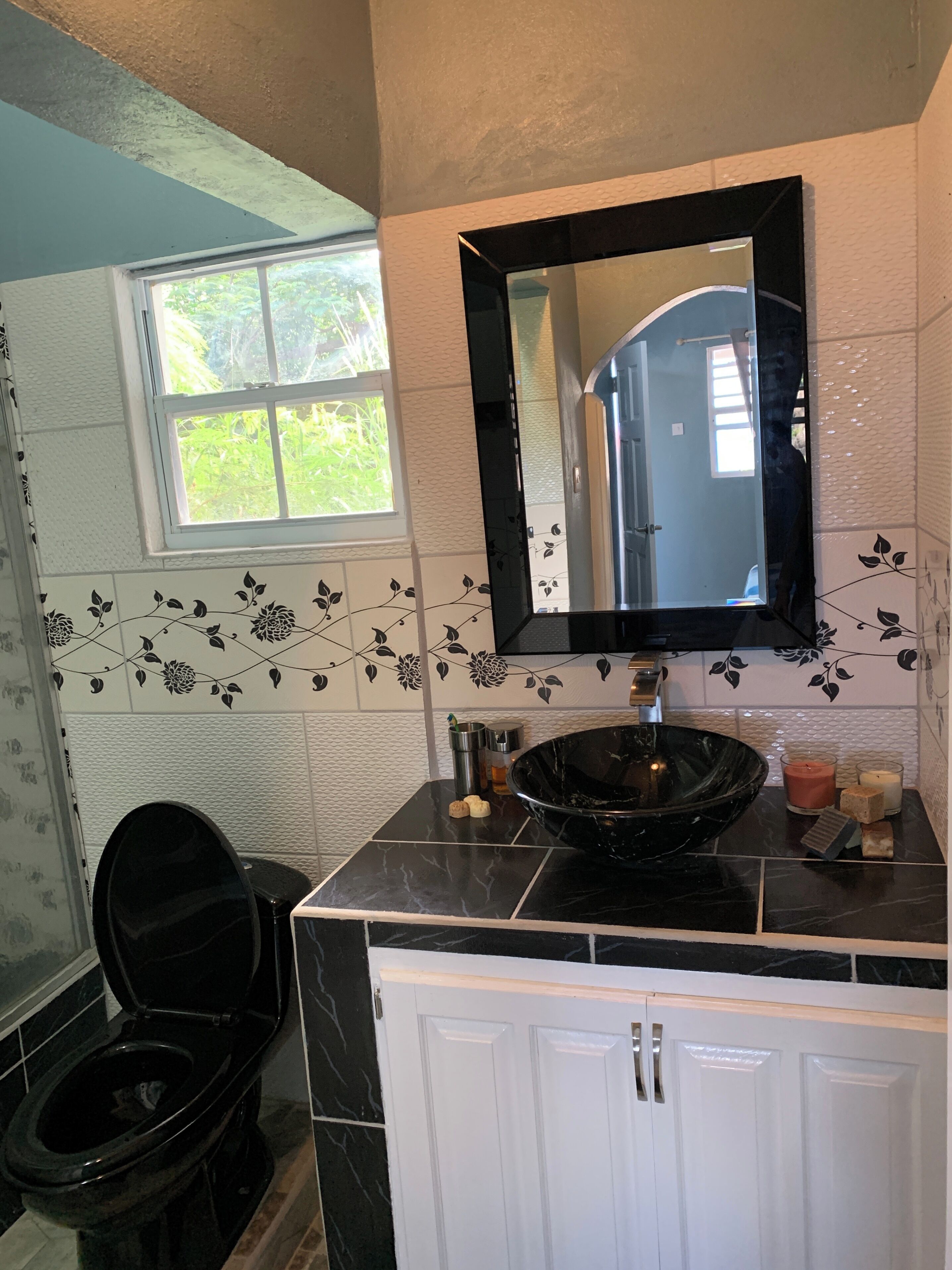 Un bagno con un lavandino nero, mobili bianchi e uno specchio sopra.