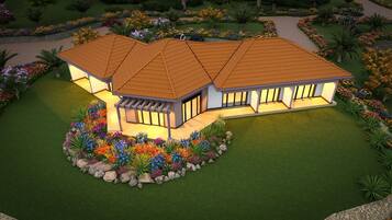 A two-story house with a tiled roof, large windows, and a landscaped garden with colorful flowers and palm trees.