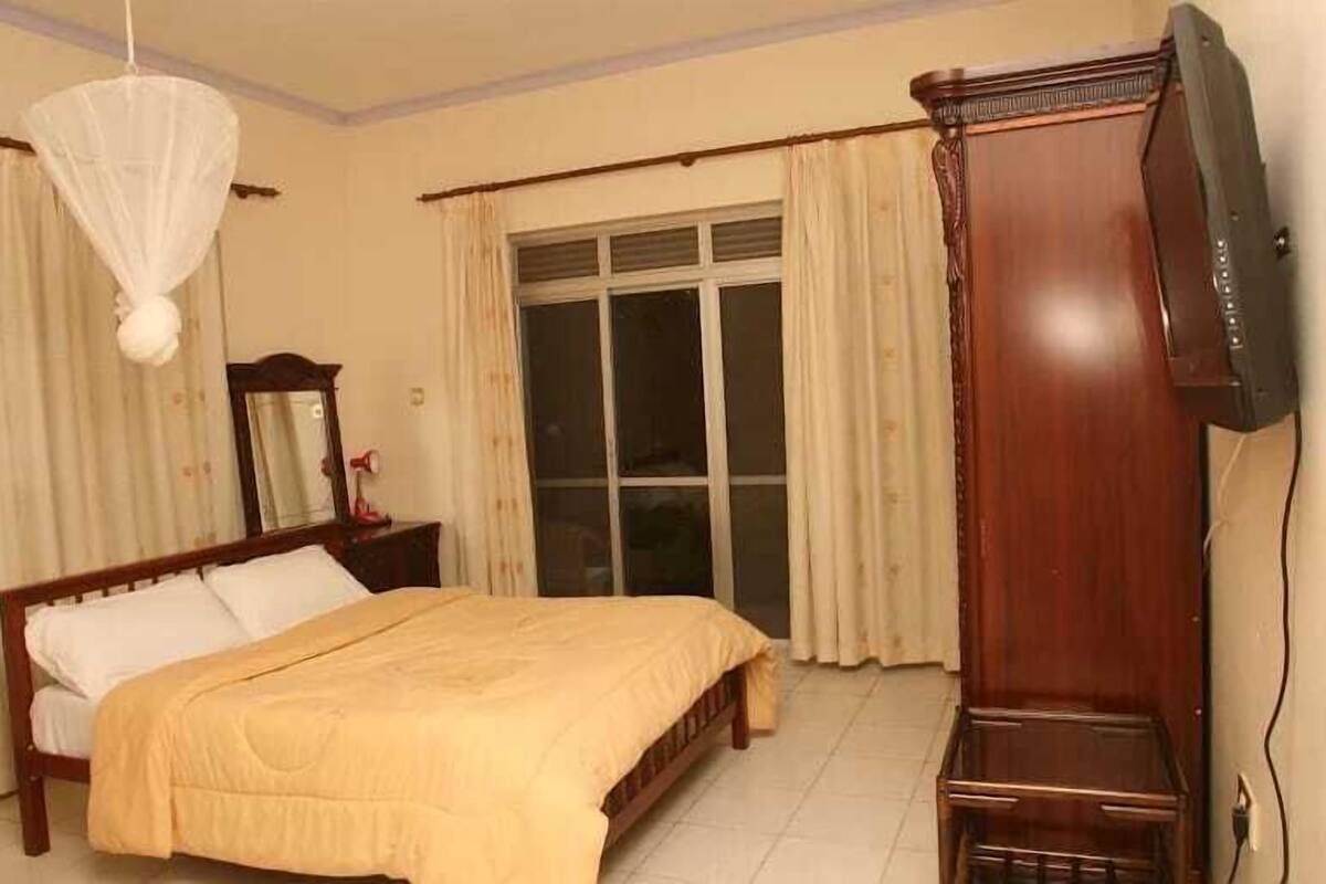 A bedroom with a bed, a television, a wardrobe, and a window with curtains.