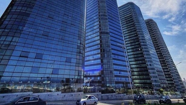 Ein modernes Hochhaus mit Glasfassade und geschwungener Form, das den Himmel und die umliegenden Gebäude widerspiegelt.