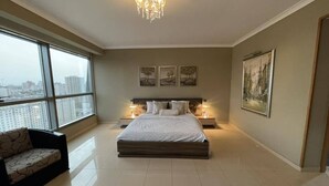Ein geräumiges Schlafzimmer mit einem großen Bett, einer Couch und Blick auf die Stadt durch große Fenster.