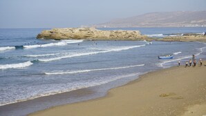 Une plage avec des vagues, un promontoire rocheux et un bateau.