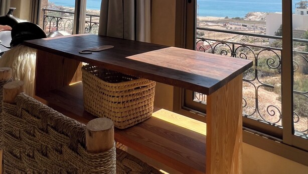 Une pièce dotée de grandes fenêtres, d’une table en bois et offrant une vue sur la mer.