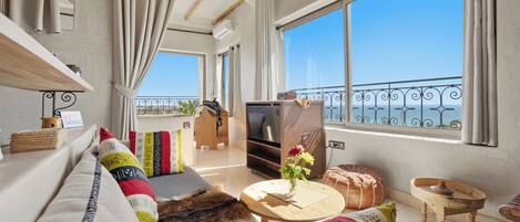 Ein modernes Wohnzimmer mit einer Couch, einem Fernseher und Blick aufs Meer.