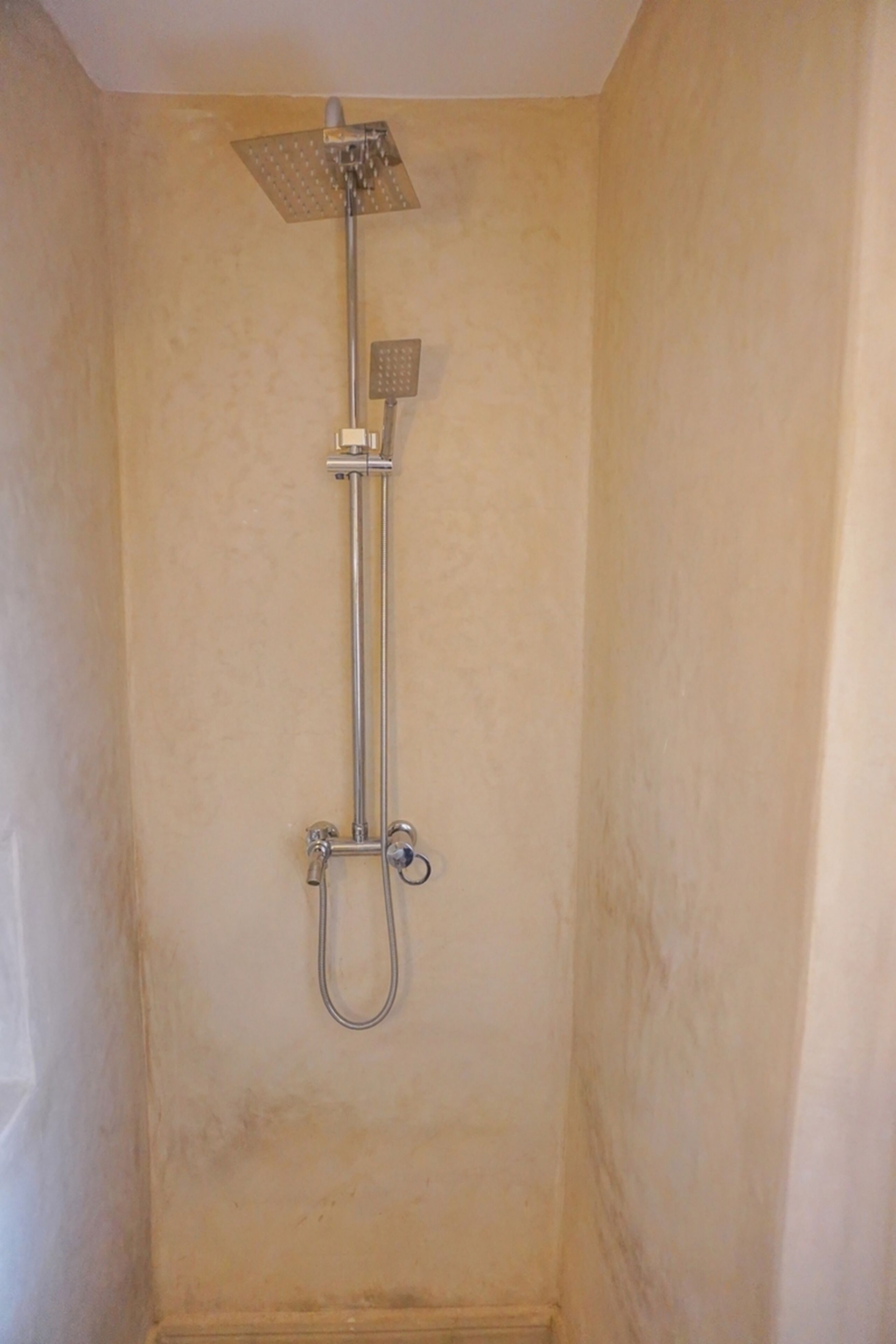 A shower with a handheld showerhead and a fixed overhead showerhead in a bathroom with beige walls.