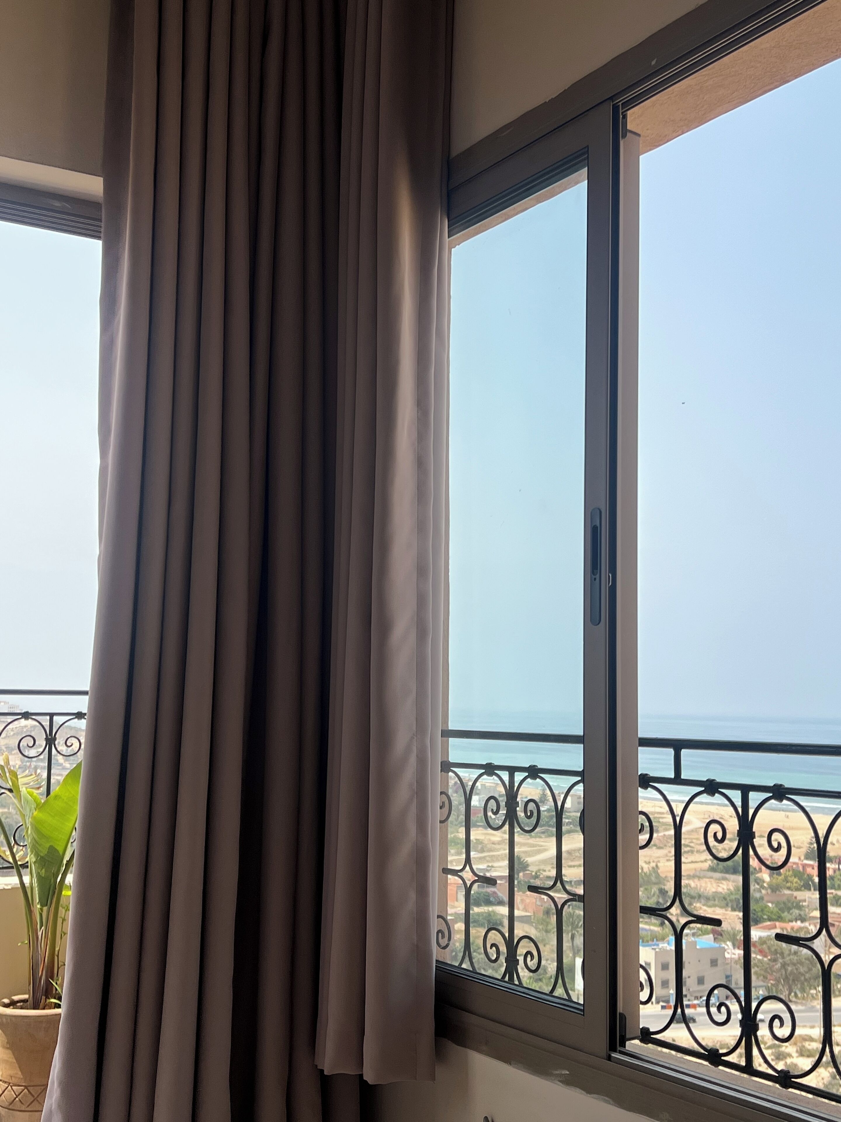 Un balcón con vista al mar, una cortina y una planta en maceta.
