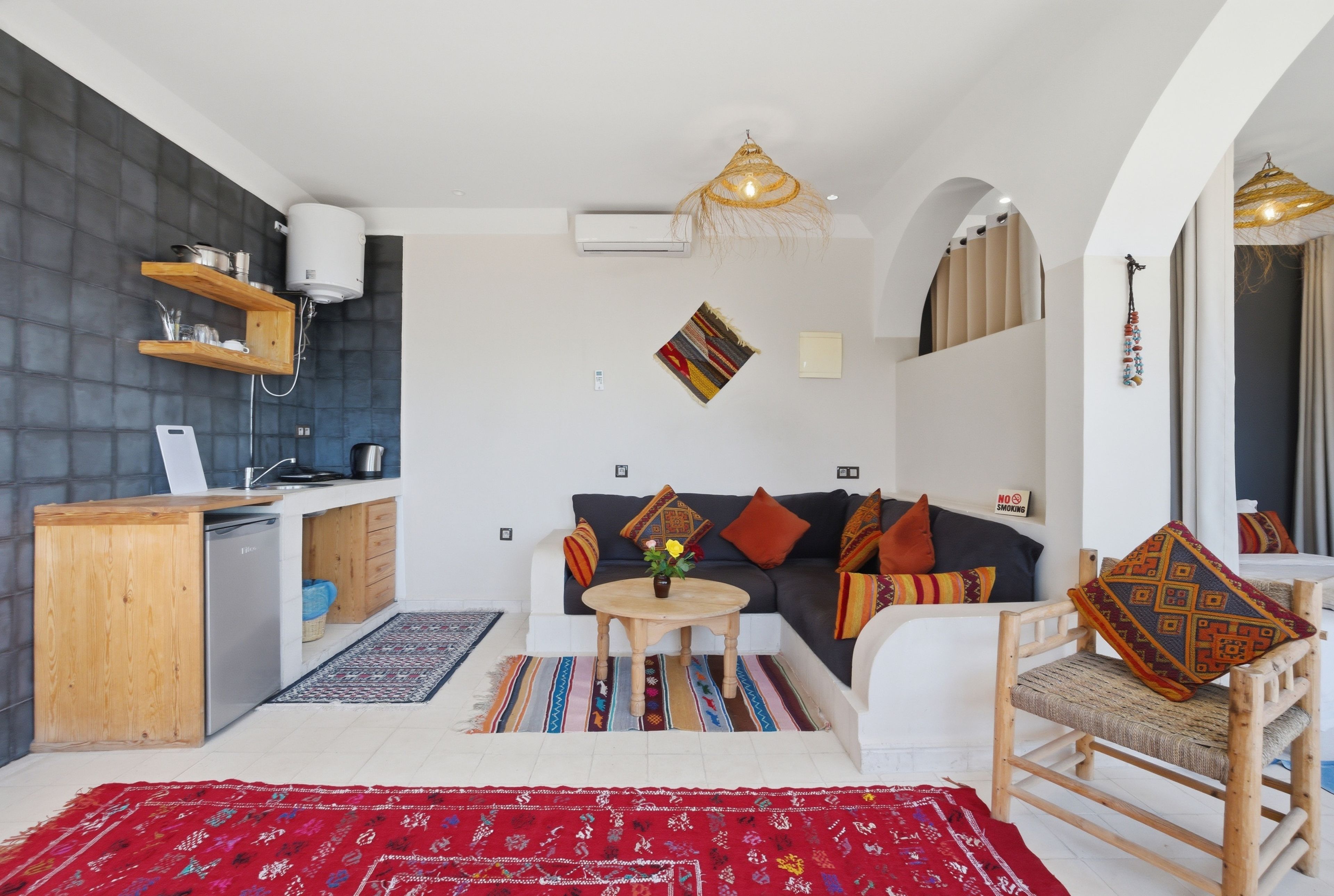 A compact living space with a kitchenette, a sofa set, a dining area, and a patterned rug.