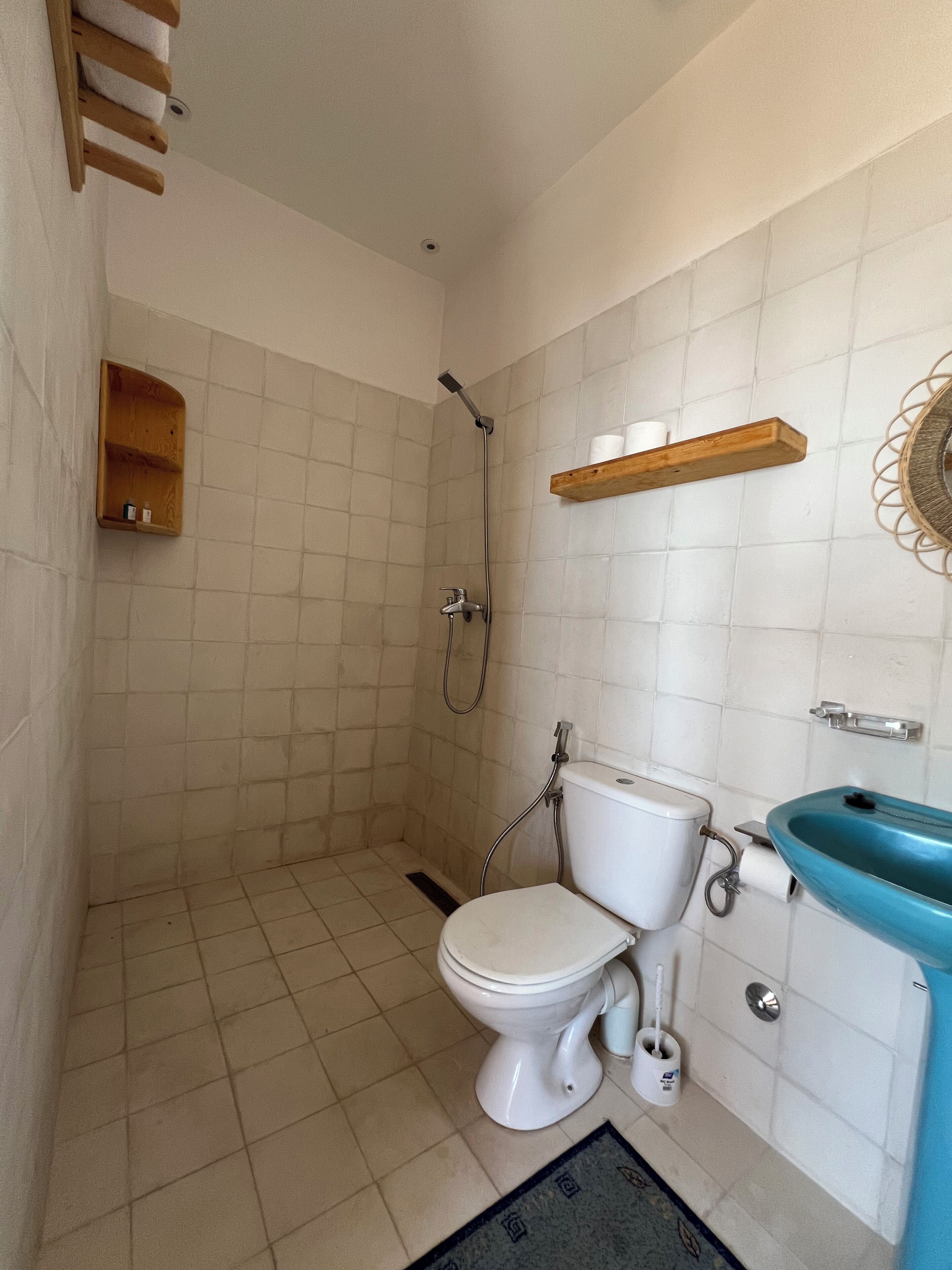 Un baño con inodoro, ducha, lavabo y estante de madera.