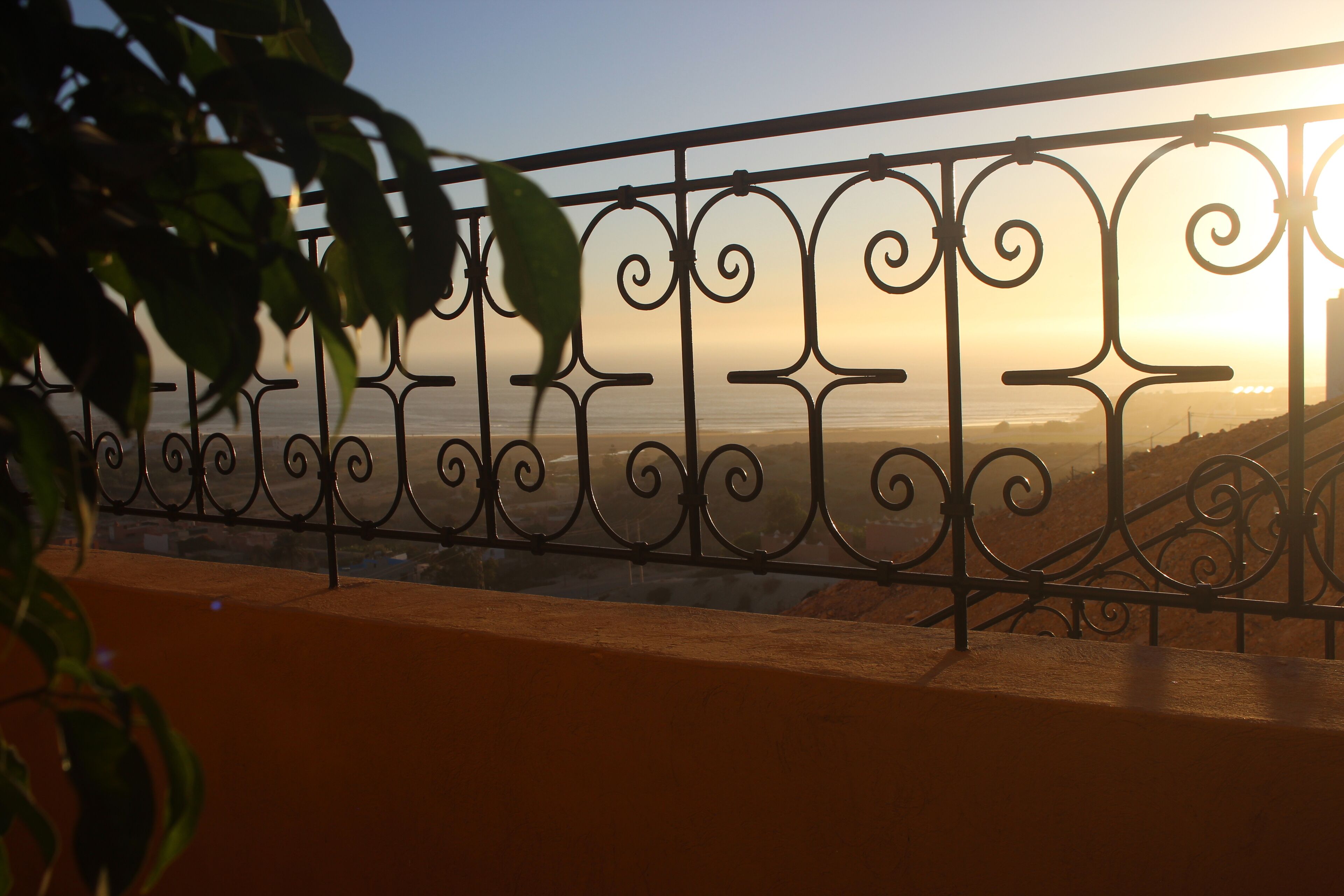 A balcony with ornate metal railings and a view of the sunset over the ocean.