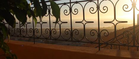 A balcony with ornate metal railings and a view of the sunset over the ocean.