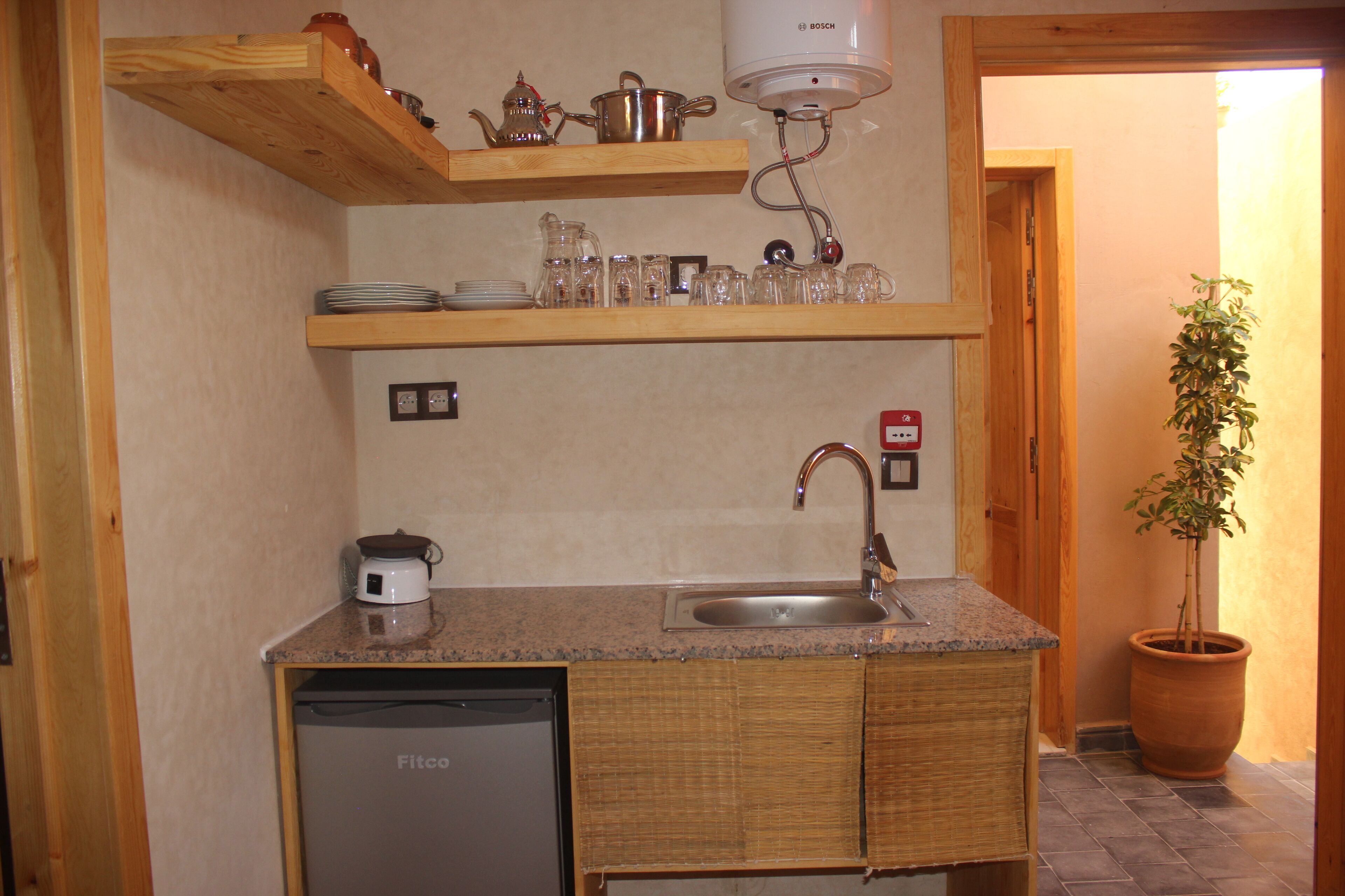 A compact kitchen with wooden shelves, a sink, and a dishwasher.