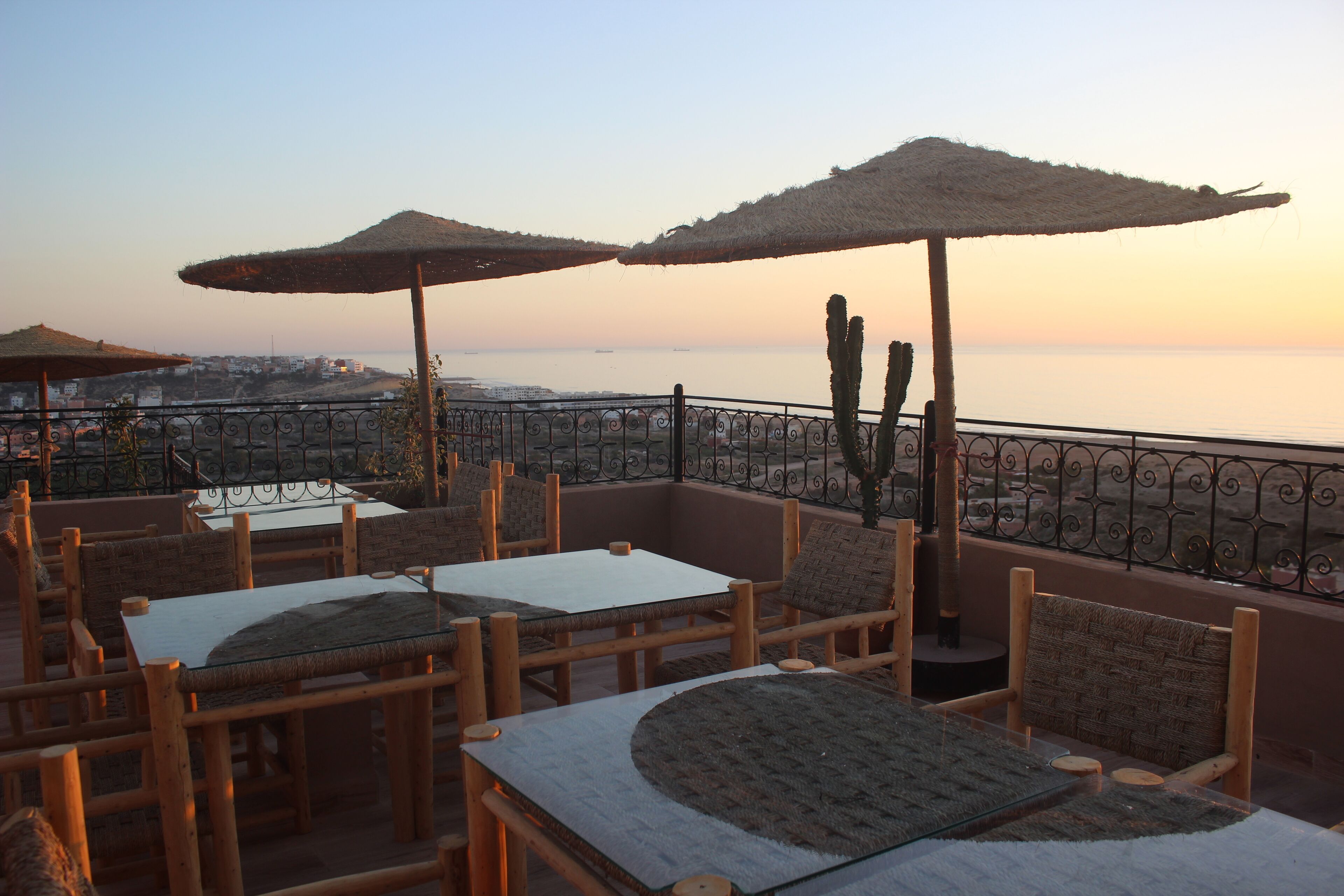 A terrace with wooden furniture and thatched umbrellas overlooking a coastal view.