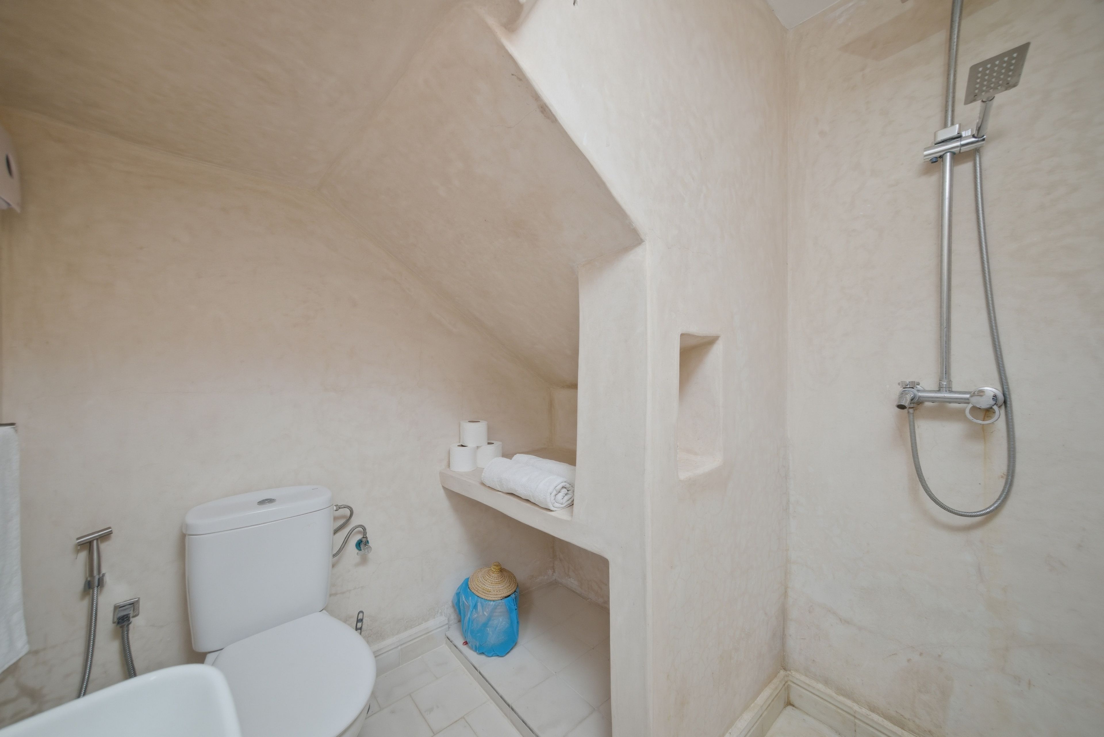 A bathroom with a toilet, bidet, and shower. There is a towel rack and a trash bin.