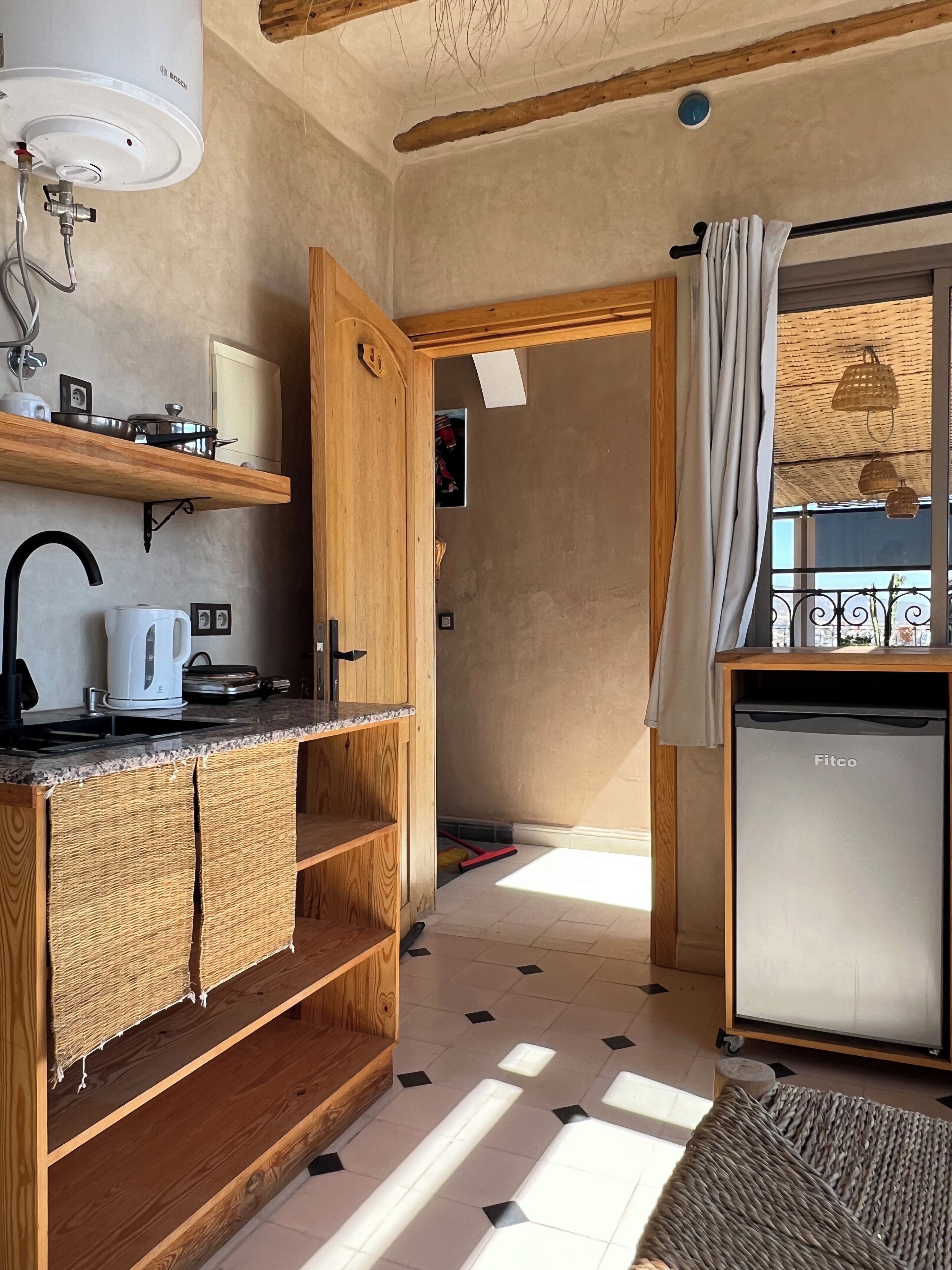 A compact kitchen with a Bosch water heater, wooden cabinets, a sink, and a Fitco refrigerator.
