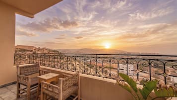 Ein Balkon mit Blick auf einen Sonnenuntergang über einer Stadtlandschaft, mit Geländer, Tisch und zwei Stühlen.