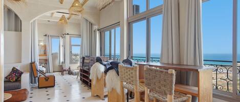 A spacious room with large windows, a wooden floor, and a view of the sea.