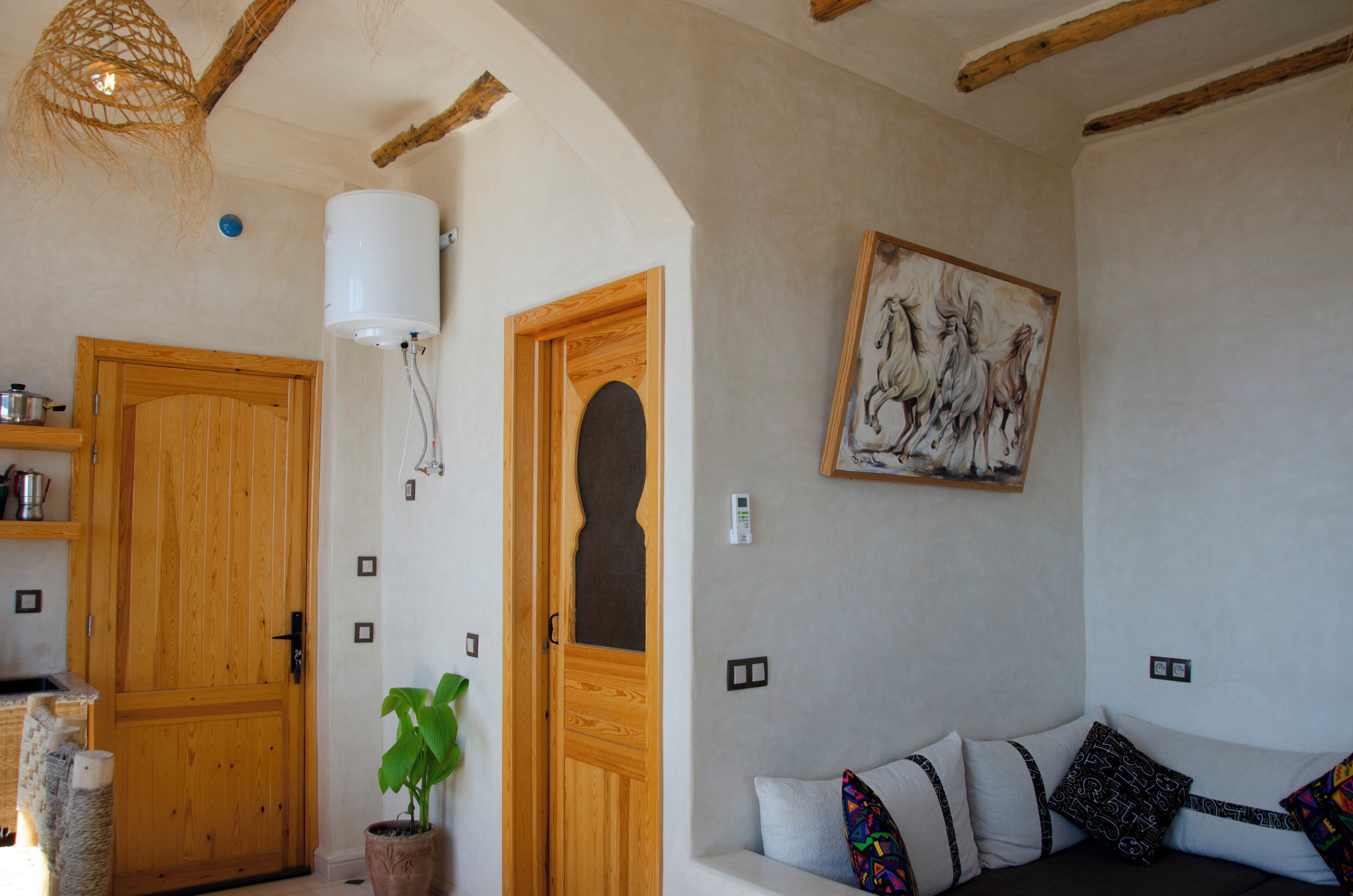 Ein gemütliches Zimmer mit Holztür, einem Topfpflanzen, einer Couch mit gemusterten Kissen und einem an der Wand hängenden Kunstwerk.