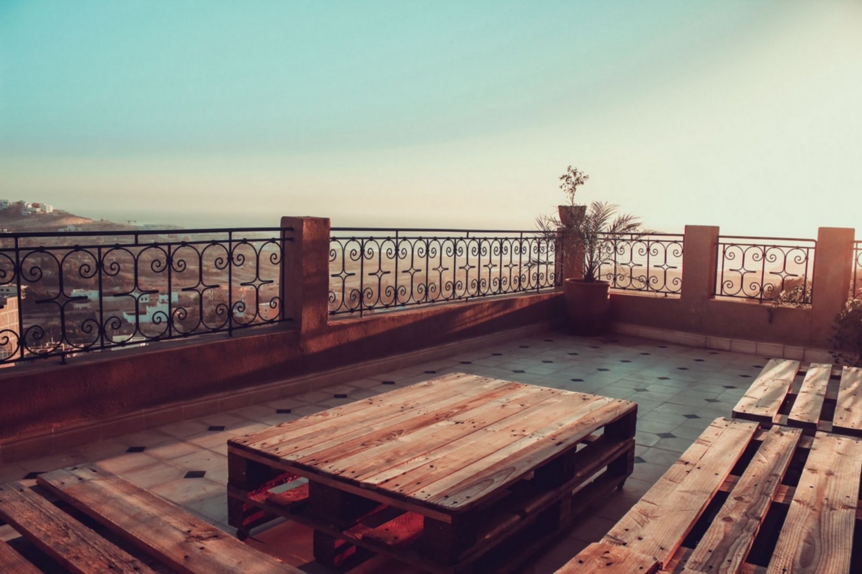 Una terraza en la azotea con mesas y bancos de madera, barandilla metálica y vistas panorámicas de la ciudad.