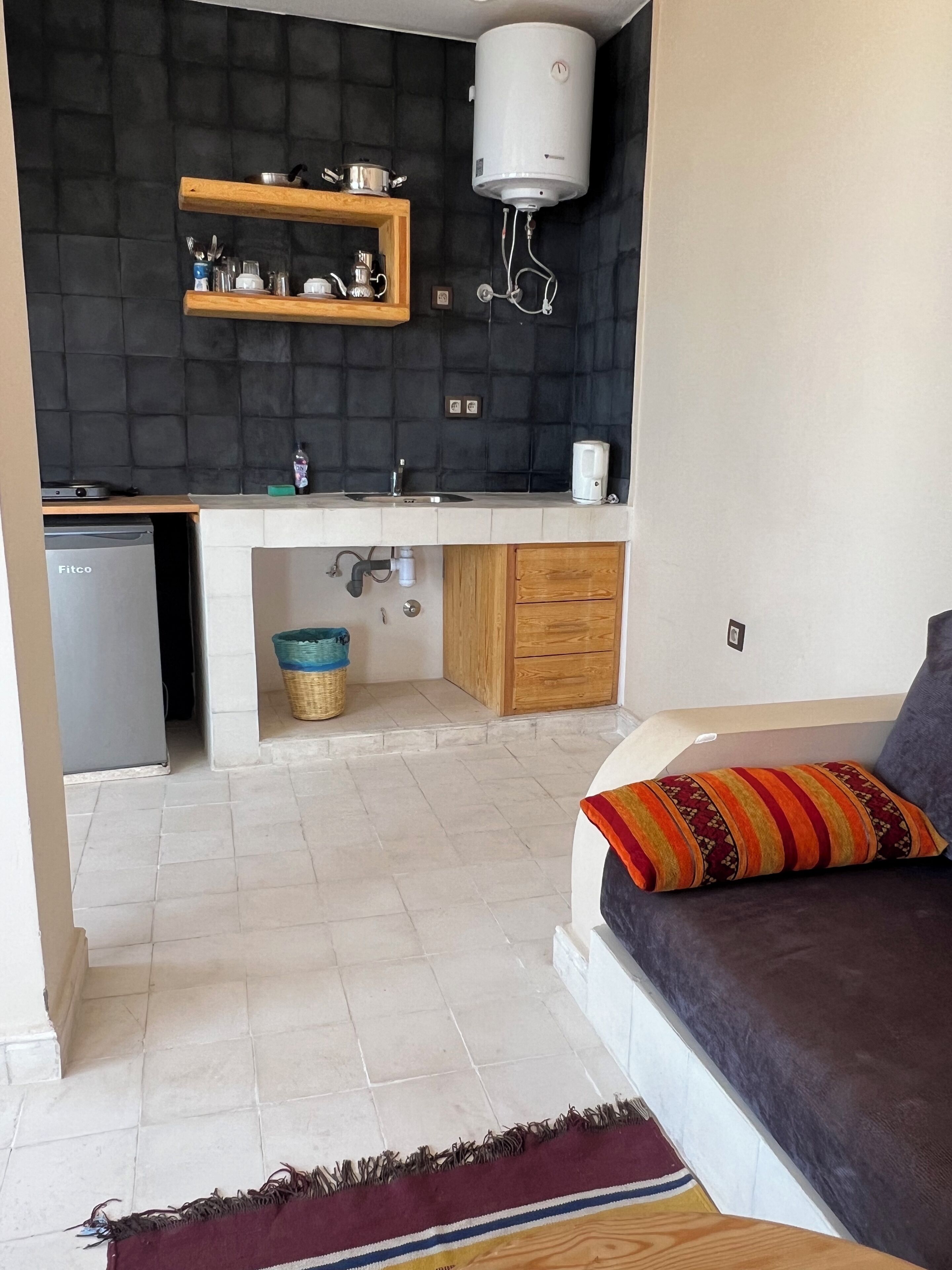 A compact kitchen with a built-in dishwasher, a water heater, and wooden shelves above the sink.