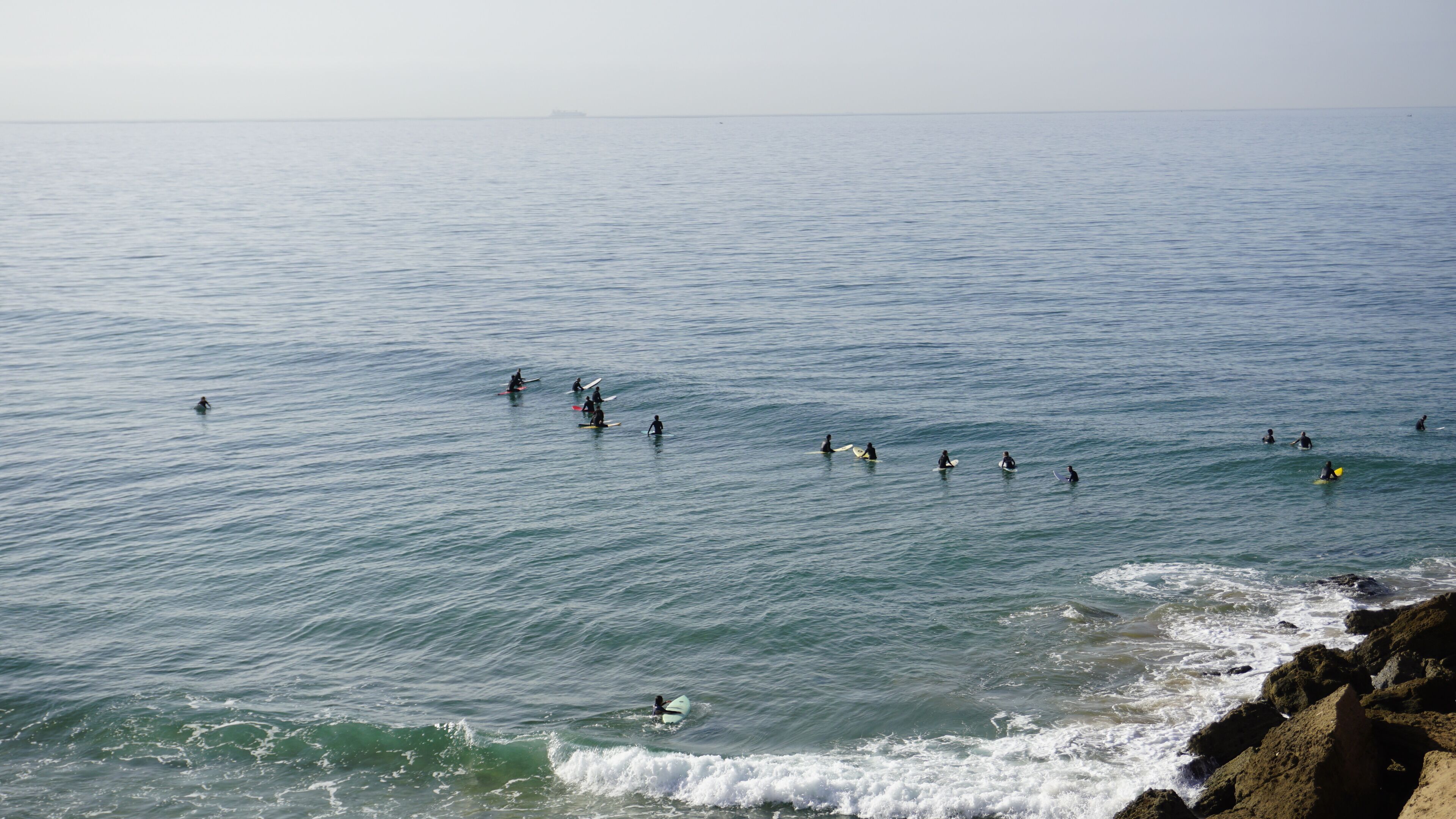 A coastal scene with surfers in the water and waves breaking near the shore.
