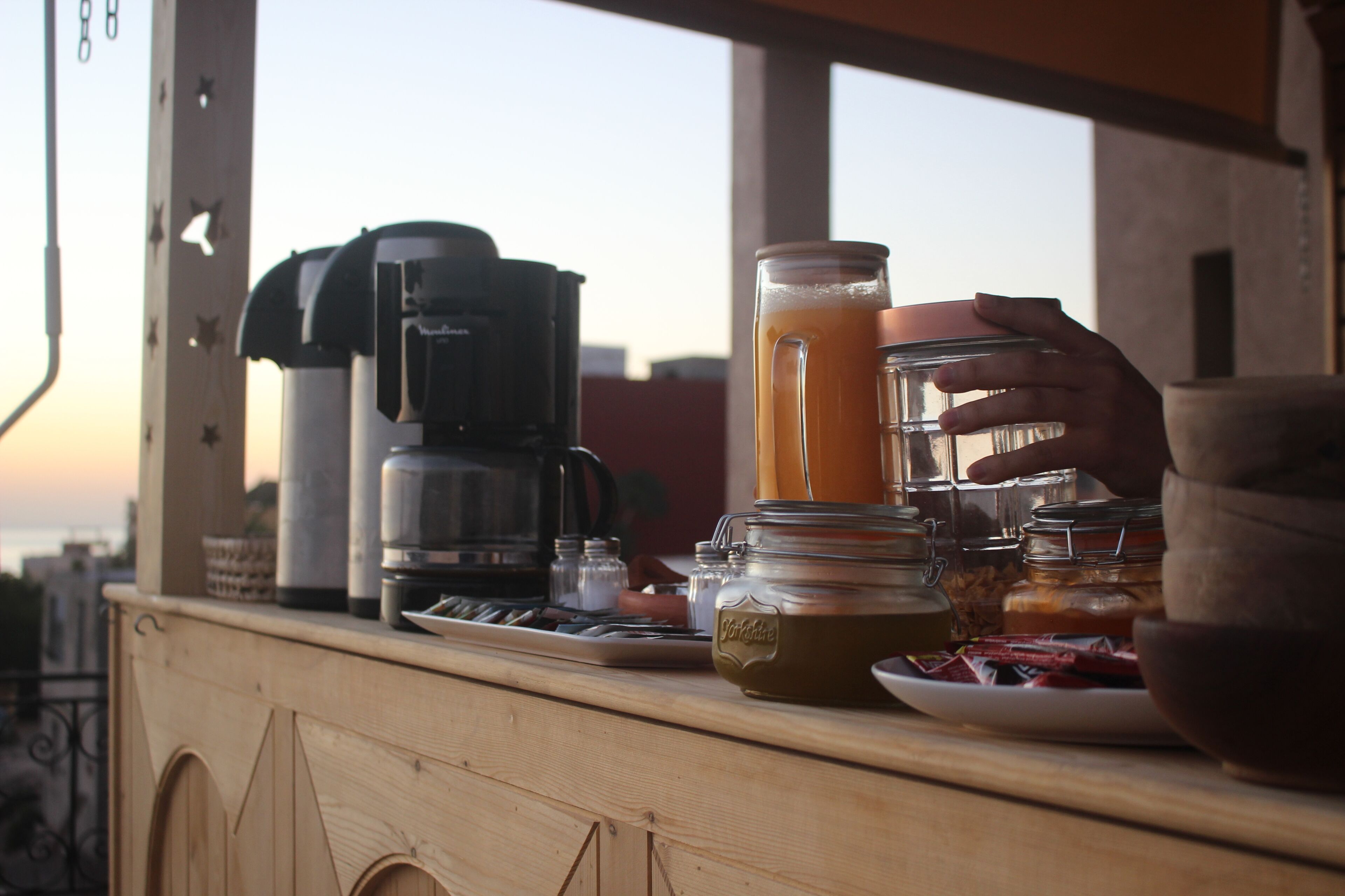 A wooden counter with a coffee maker, a glass of orange juice, and various jars and bowls.