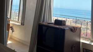 Une pièce dotée d’une grande fenêtre donnant sur la mer, d’un plafond rustique et d’un téléviseur posé sur un meuble en bois.