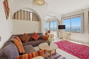 Una sala de estar con sofá, mesa de centro, televisor y vista al cielo.