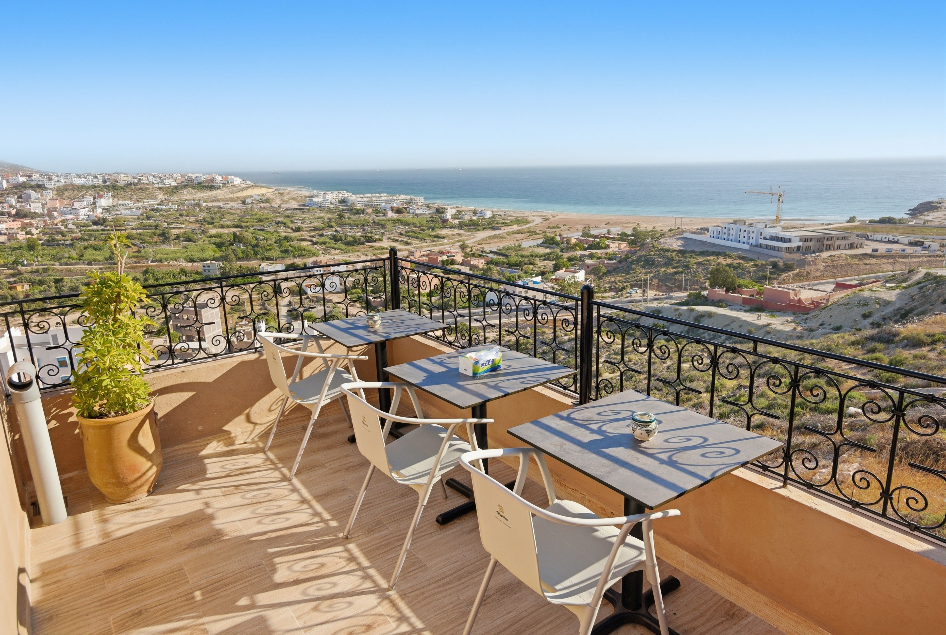 A terrace with tables and chairs overlooking a coastal cityscape.