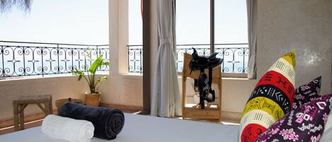 A hotel room with a bed, a potted plant, a wooden stool, and a balcony with a railing.