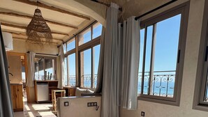Une chambre spacieuse avec un grand lit, un petit bureau et une vue sur la mer grâce à de grandes fenêtres.