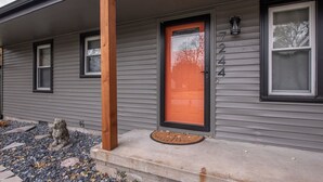 A house with a gray siding exterior, a wooden porch, a red door with the number 7244, and a small stone statue on the porch.