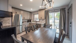 A modern kitchen with stainless steel appliances, a dining area with a large table and chairs, and a view of the outdoors through a sliding glass door.