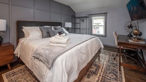 A bedroom with a bed, a desk, a ceiling fan, and a window.