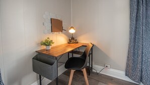 Un espacio de trabajo reducido con un escritorio de madera, una silla negra, una pequeña planta en maceta y un espejo hexagonal fijado a la pared.